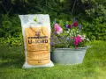 En säck U-jord från Hasselfors Garden står bredvid en zinkbalja fylld med färgglada blommor, redo att plantera.