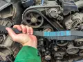A hand holds a new Dayco drive belt, ready for replacement on a car engine.
