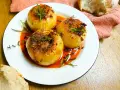 Tres cebollas al horno, rellenas y doradas, nadan en una salsa roja vibrante. Hierbas frescas coronan cada una.