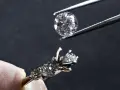 Un diamante viene posizionato con una pinzetta su un anello con incastonatura a castone ribattuto, pronto per essere fissato.