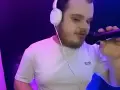 Młody dj akun w słuchawkach i białej koszulce z mikrofonem w ręku, w studiu z fioletowym oświetleniem.
