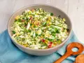 Schüssel mit knackigem Salat aus Weißkohl, Mais, Erbsen und Paprika, perfekt als salate zum vorbereiten am vortag. Mit frischer Petersilie garniert.