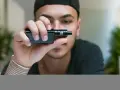 Joven con gorra negra sostiene un cigarrillo electrónico, mostrando sus claromizadores.