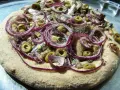 Pizza z anszua, oliwkami i czerwoną cebulą, gotowa do pieczenia.