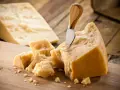 Kawałki Grana Padano i parmezanu na drewnianej desce. Nóż wbity w duży kawałek sera.
