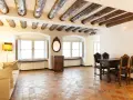 Stary salon z belkami stropowymi i podłogą z terakoty. Kanapa, stół z krzesłami i komoda tworzą przytulną atmosferę.