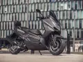 Ciemnoszary skuter Zipp QR Max 125 z czarną tapicerką i czerwonymi przeszyciami, zaparkowany przed nowoczesnym budynkiem.