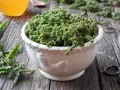 Schale mit Brennesselsamen, die ihre positive brennesselsamen wirkung für die Gesundheit andeuten. Daneben ein Glas mit gelber Flüssigkeit.