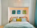 Idee salvaspazio camera da letto piccola: letto con testiera contenitore, quadri colorati e tende turchesi creano un ambiente accogliente.