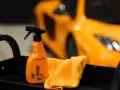 En orange sprayflaska för att ta bort limrester och insekter, bredvid en orange mikrofiberduk. En sportbil i bakgrunden.