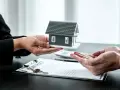 Manos entregan maqueta de casa sobre contrato y llaves. Posible exención IRPF venta vivienda heredada.