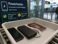Na lotnisku, w tacce bezpieczeństwa leżą telefon, powerbank i paszport. Tablica informuje o limicie mocy powerbanków w bagażu podręcznym, np. dla Ryanair.