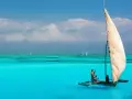 Zanzibar w kwietniu: błękitne morze, białe chmury i tradycyjna łódź z żaglem. Idealna pogoda na rejs.