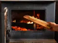 Ręka wkłada do paleniska świeże drewno, które jest kluczowe dla określenia jaka wilgotność drewna do kominka zapewni efektywne spalanie.