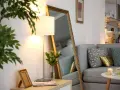 Ein großer Spiegel und eine Stehlampe helfen, die dunkle Wohnung heller zu machen. Ein Sofa mit Kissen und ein kleiner Tisch vervollständigen die Szene.