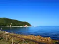 A tranquil bay in Tuscany with sailboats docked, a green hillside, and a rustic wooden fence in the foreground.