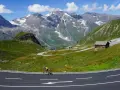 Rowerzysta na krętej drodze w Alpach, z majestatycznymi szczytami w tle. To idealne miejsce na podróż szwajcaria motocyklem.