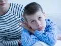 Bambino con sguardo pensieroso, forse durante un test autismo bambini 2 anni. La madre lo osserva con preoccupazione.