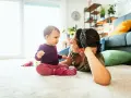 Mama patrzy na dziecko, które siedzi na dywanie. To obrazek pokazujący, co powinien umieć 2 latek: rozwijać się i bawić.
