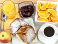 Pyszne śniadanie kontynentalne: rogaliki z cukrem pudrem, pomarańcze, dżem, sok i kawa.
