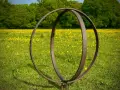 Metallskulptur im Feld mit gelben Blumen. Eine Idee, wie man ein Rondell im Garten gestalten kann, mit rustikalem Charme.