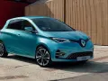 Błękitny Renault Zoe z nowoczesnymi światłami LED stoi na tle drewnianej elewacji.