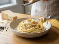Un plato de cacio e pepe cremoso, con queso rallado cayendo sobre los espaguetis y granos de pimienta negra.