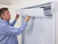 Un homme ajuste le tablier d'un volet roulant. Il montre comment relever un volet roulant électrique sans électricité.