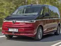 Nowy Volkswagen van w kolorze czerwono-czarnym pędzi po drodze, otoczony zielenią drzew.