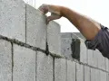 Pose d'un parpaing pour un mur de 25m. Le maçon ajuste la brique avec précision.