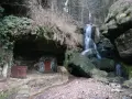 Ein versteckter Wasserfall bei Bad Schandau, mit einer kleinen Höhle und einer roten Tür.