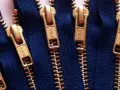 Primer plano de varias partes de una cremallera YKK dorada sobre tela azul.