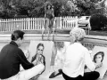 Konstnärer målar vid poolen, en kvinna i baddräkt klättrar upp ur vattnet. Kanske inspirerade av Walter Keane.