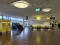 Żółte automaty biletowe Arlanda Express na lotnisku w Sztokholmie. W tle ruchome schody i znaki kierujące.