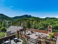 Hotel z widokiem na góry. Taras z meblami i leżakami, otoczony zielenią i górami.