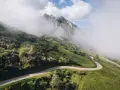 Strada tortuosa che sale verso le vette nebbiose, evocando l'ascesa al **Col du Tourmalet**.