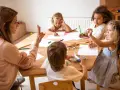 Bambini disegnano e giocano con un aereo, guidati da un'insegnante. Un esempio di come le scienze della formazione sbocchi in attività creative e formative.