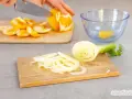 Frischer Fenchelsalat wird zubereitet. Eine Person schneidet Orangen, während Fenchelscheiben auf einem Holzbrett liegen.