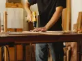 Mann bohrt Holzbretter, um seine Werkstatt einzurichten. Hobelspäne liegen auf dem Tisch.