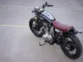 Klasyczny motocykl Yamaha z brązowym siedzeniem i gwiazdą na baku. Kraj pochodzenia tego modelu to Japonia.