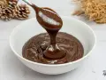 Cuchara con ganache de chocolate cayendo en un cuenco blanco. El chocolate es brillante y sedoso, perfecto para postres.