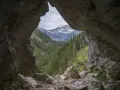 Widok z jaskini w Tatrach na ośnieżone szczyty i gęsty las.