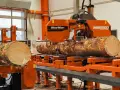 Pomarańczowa maszyna do obróbki drewna Wood-Mizer WM2500 przetwarza pień drzewa na deski.