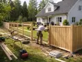 Man bygger staket runt ett vitt hus. Verktyg och material ligger utspritt på gräsmattan.