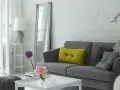 Sofá gris con cojines, espejo alto y lámpara. Trucos para decorar espacios pequeños con estilo y amplitud.