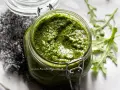 Un vasetto di pesto di rucola fatto in casa, con foglie di rucola fresca sullo sfondo.