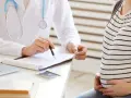 Lekarz omawia z ciężarną pacjentką kolejne trymestry ciąży, notując coś na dokumentach.