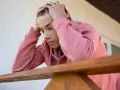 Nastolatek z rękami wplątanymi we włosy, zamyślony. Objawy silnego stresu u nastolatków mogą być widoczne w jego postawie.