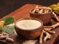 Drewniane miseczki z proszkiem i korzeniami ashwagandhy, liście, owoce i kapsułki.
