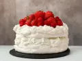 Puszysty tort bezowy z bitą śmietaną i mnóstwem świeżych truskawek i malin. Idealny na letnie popołudnie.
